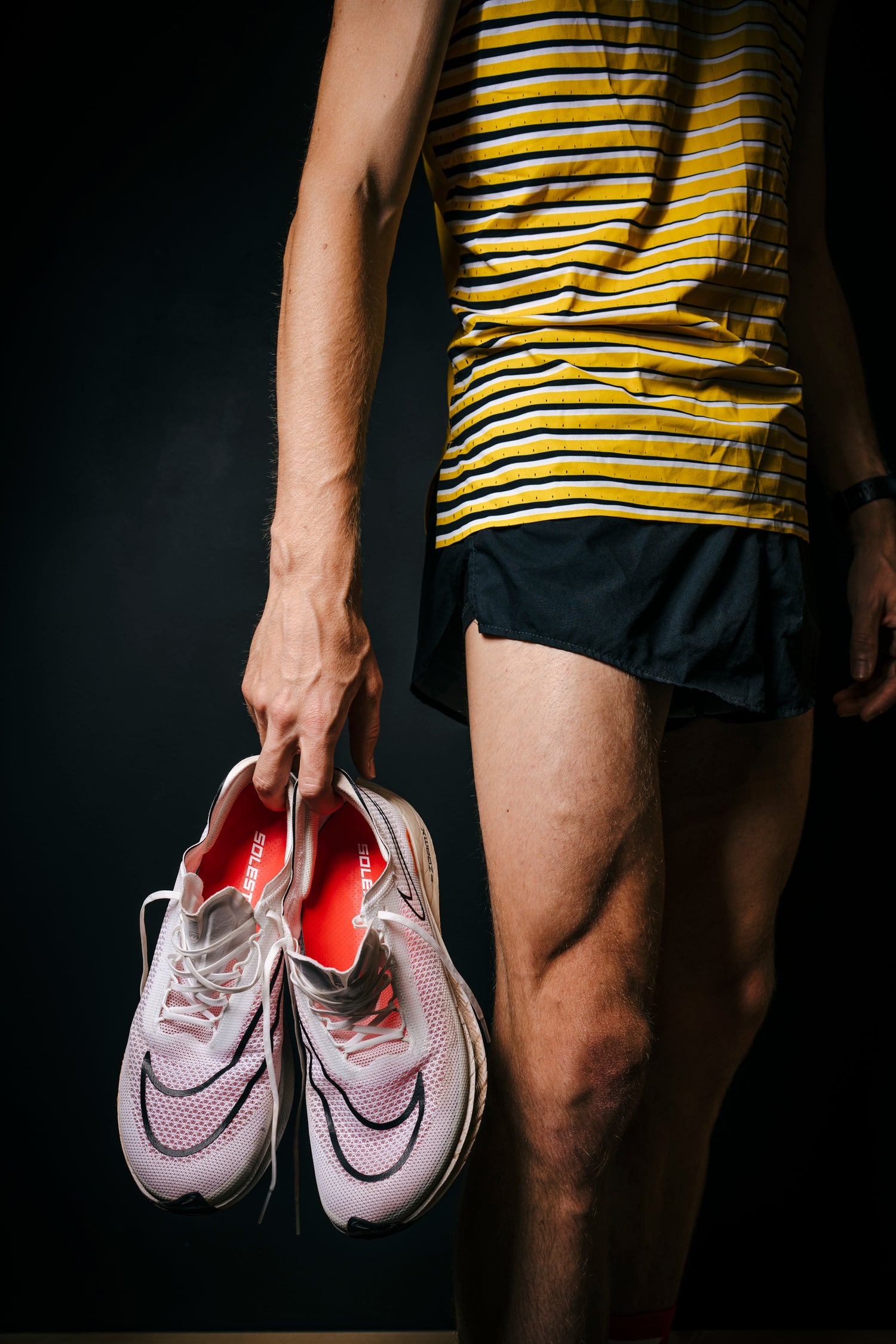 Person in athletic wear holding pink sneakers against a dark background