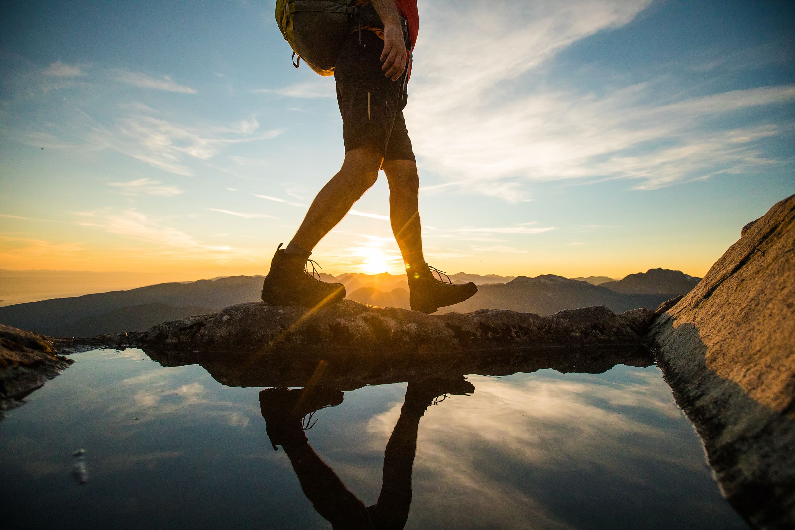 Professional hiker walking on rocks with a sunset in the background.