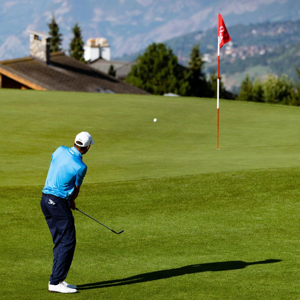 Golfer taking a swing on a green golf course with mountains in the background