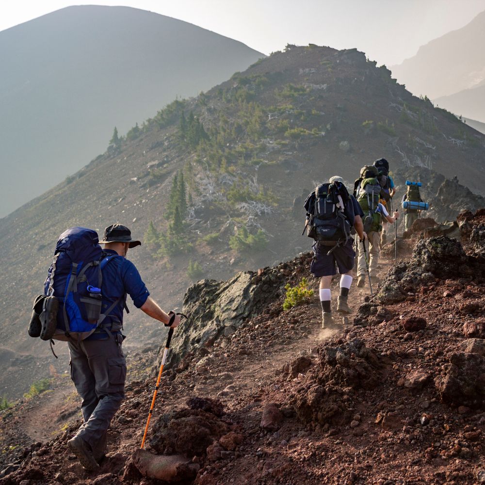 Group of hikers climbing a rocky mountain trail with mountains in the background.