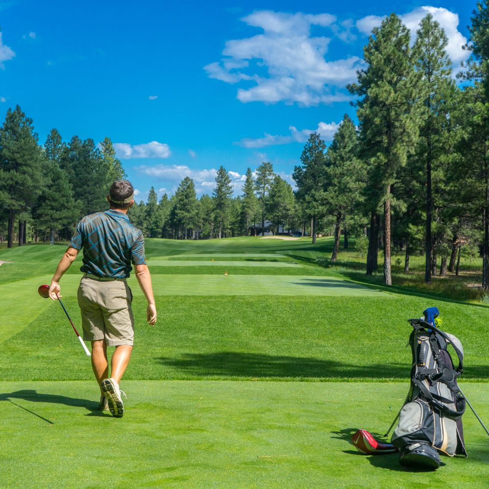 Man walking on a golf course with trees and blue sky in the background