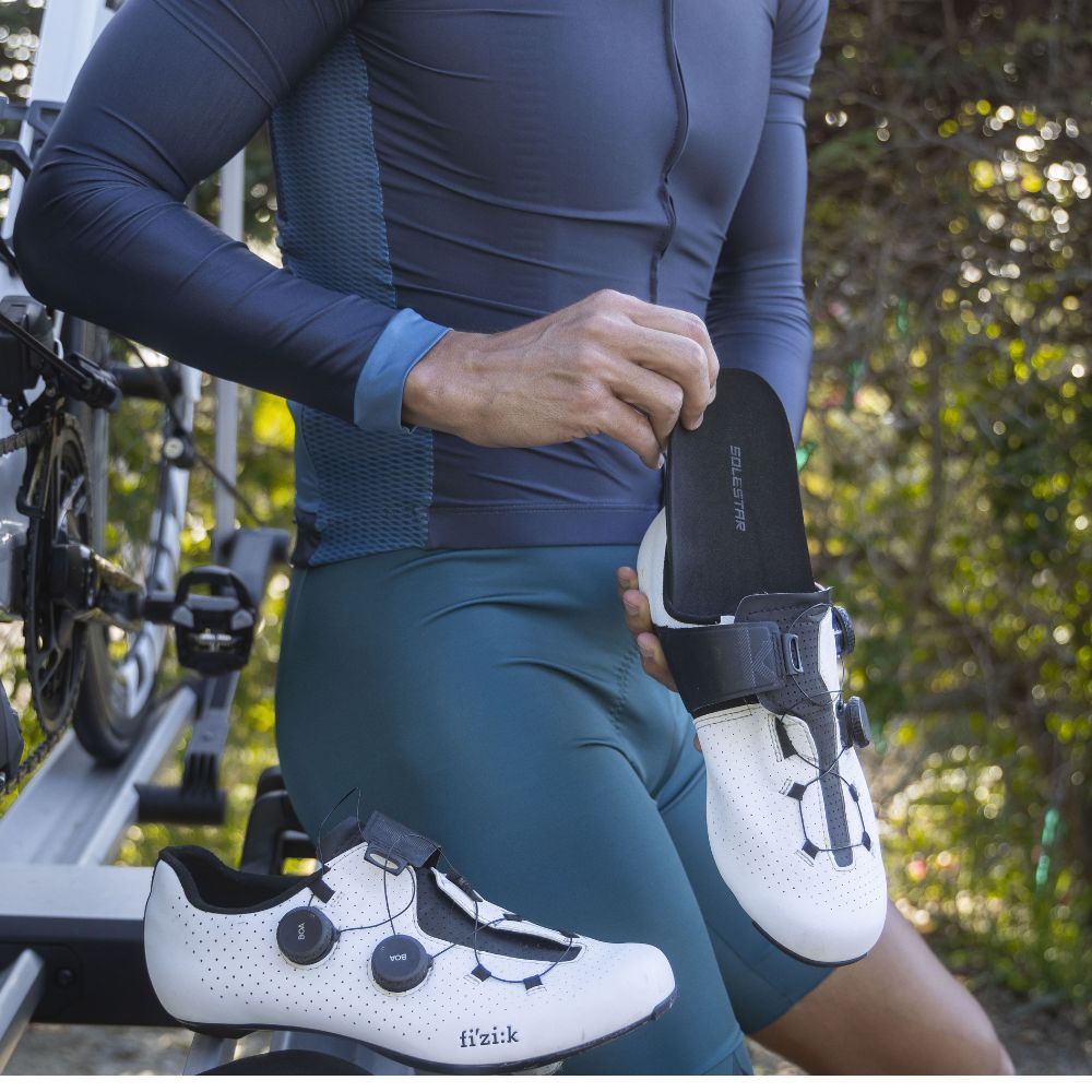 Person wearing cycling shoes and holding a bike in a forest setting