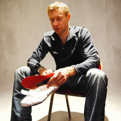 Jens Voigt sitting on a chair holding a SOLESTAR KONTROL Insole, wearing a dark jacket with logos.