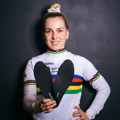 Emma Hinze wearing a cycling outfit with rainbow stripes holding cycling insole in a dark background