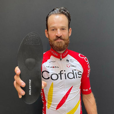 Pro cyclist Simon Geschke
 in cycling jersey holding a solestar insole against a dark background