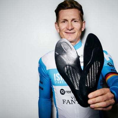 Pro cyclist André Greipel  in cycling jersey holding a black shoe insoles with tread pattern against a white background