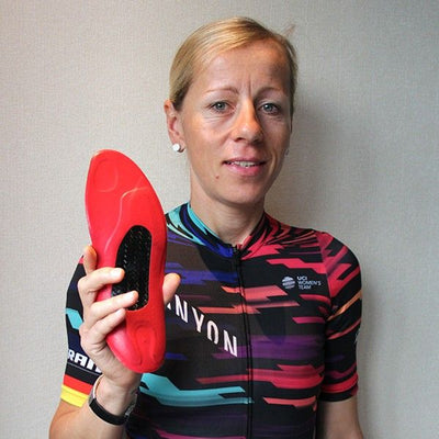 Trixi Worrack wearing a colorful cycling jersey holding a red shoe insole against a plain background