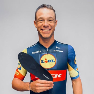 Pro Cyclist Jonathan Milan in a colorful jersey holding a SOLESTAR BLK insole against a gray background