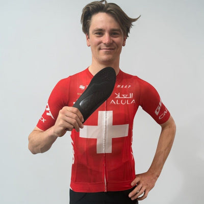 Pro Cyclist Mauro Schmid wearing a red cycling jersey with a Swiss cross design, holding a black solestar insole.